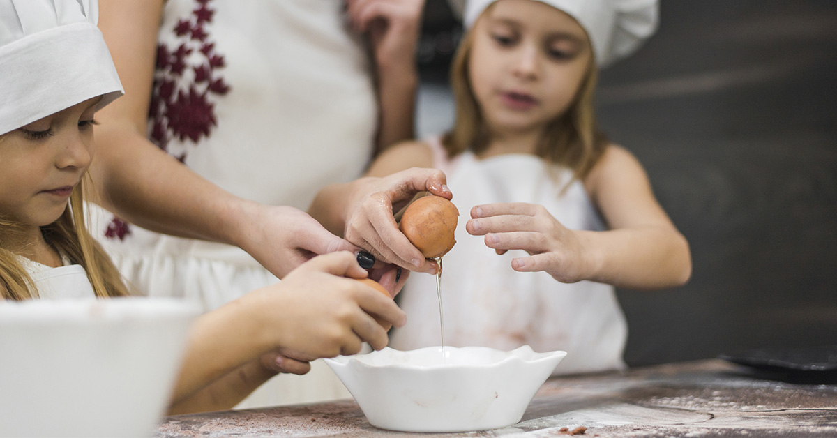 ninos cascando un huevo con ayuda de un adulto